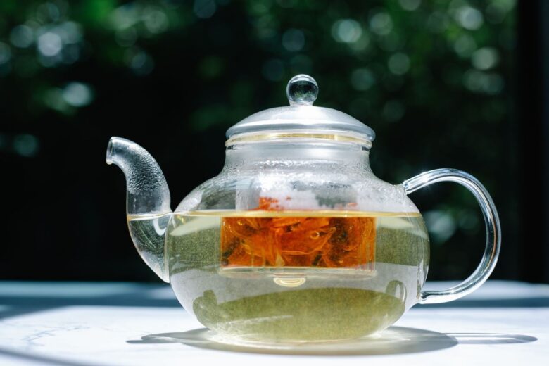 Théière en verre contenant une infusion ambrée et des ingrédients végétaux